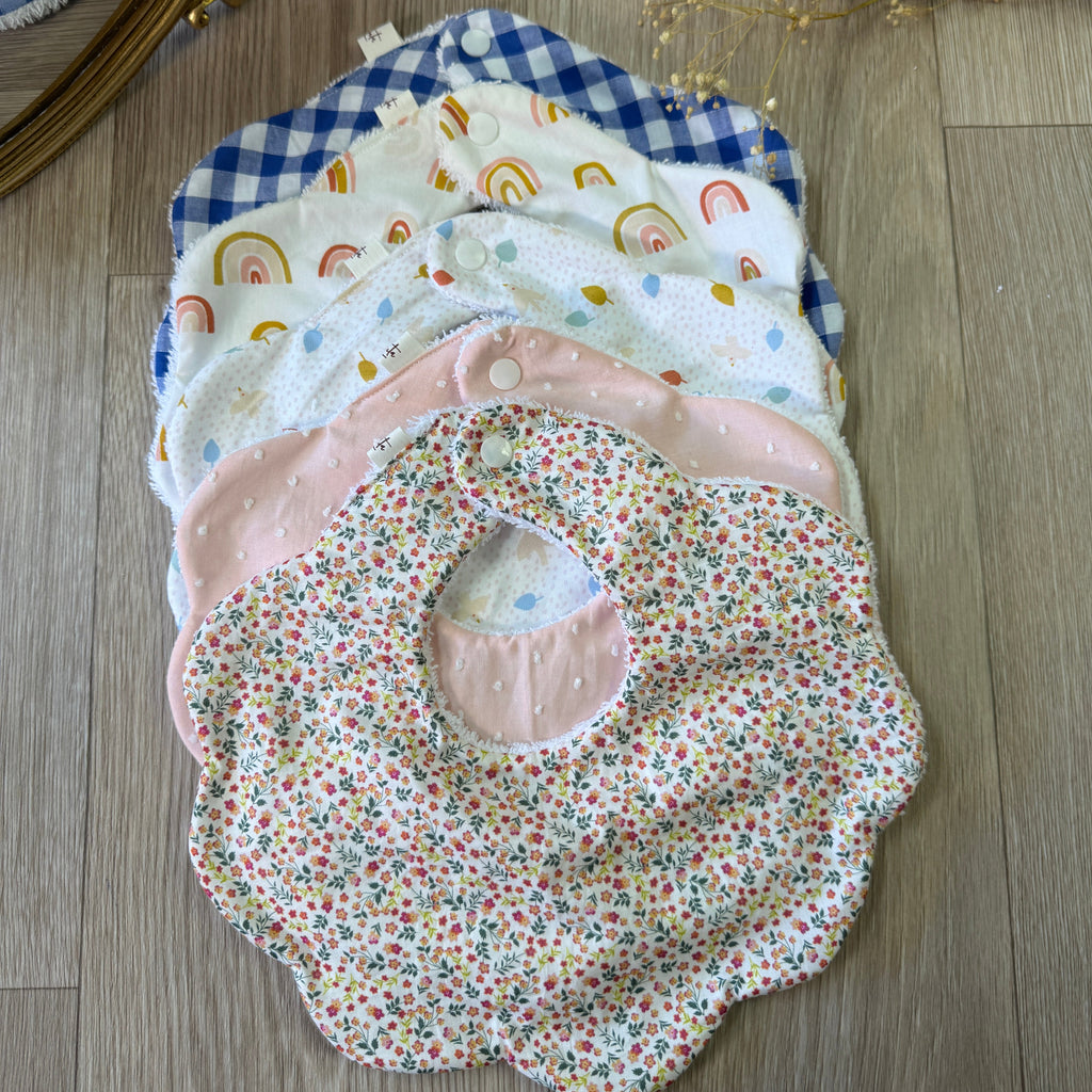 coffret de 5 bavoirs forme fleurs en coton et double gaze à motifs posés sur un parquet