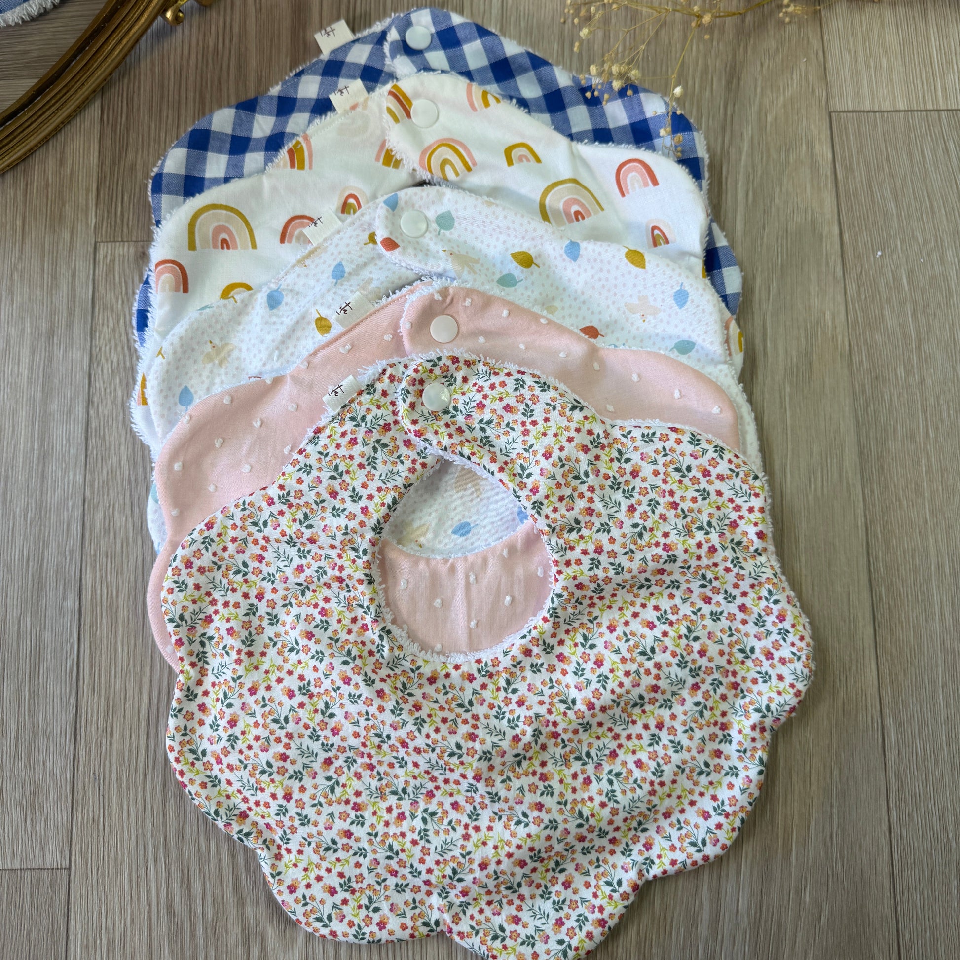 coffret de 5 bavoirs forme fleurs en coton et double gaze à motifs posés sur un parquet